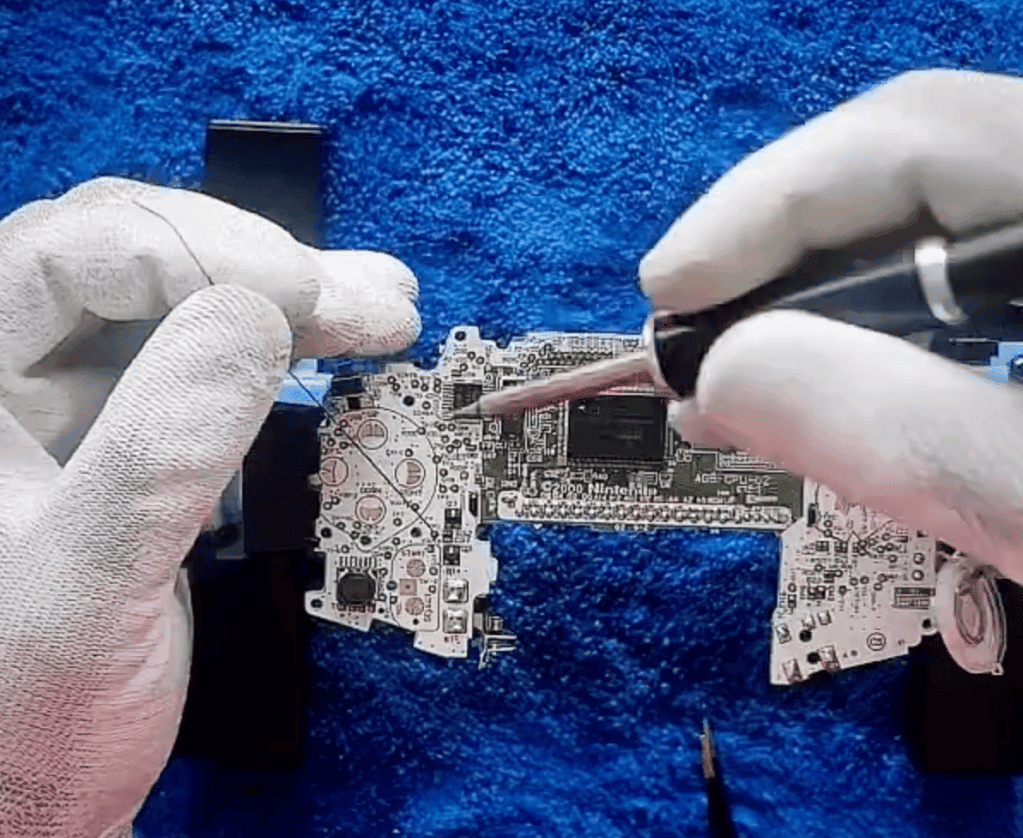 RetroGear modding technician soldering a Nintendo Game Boy Advance motherboard while wearing white gloves.